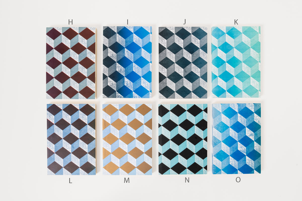Stack of Astier de Villatte medium notebooks with geometric patterns in gold, blue, and black colors.