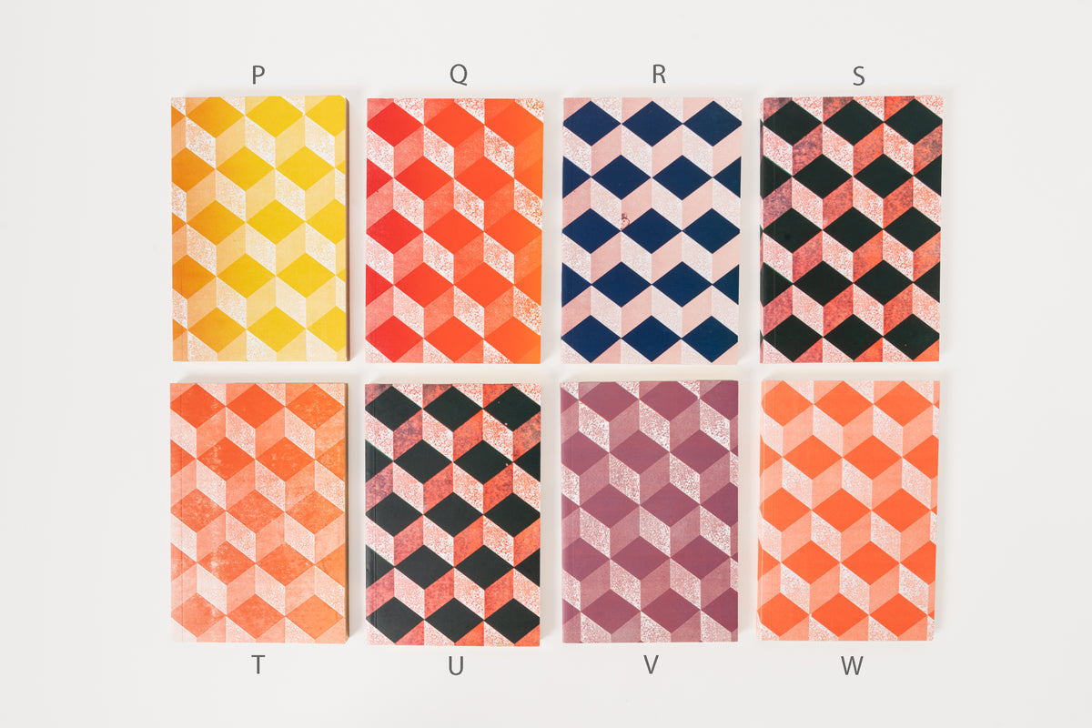 Stack of Astier de Villatte medium notebooks with geometric patterns in yellow, blue, and pink colors.