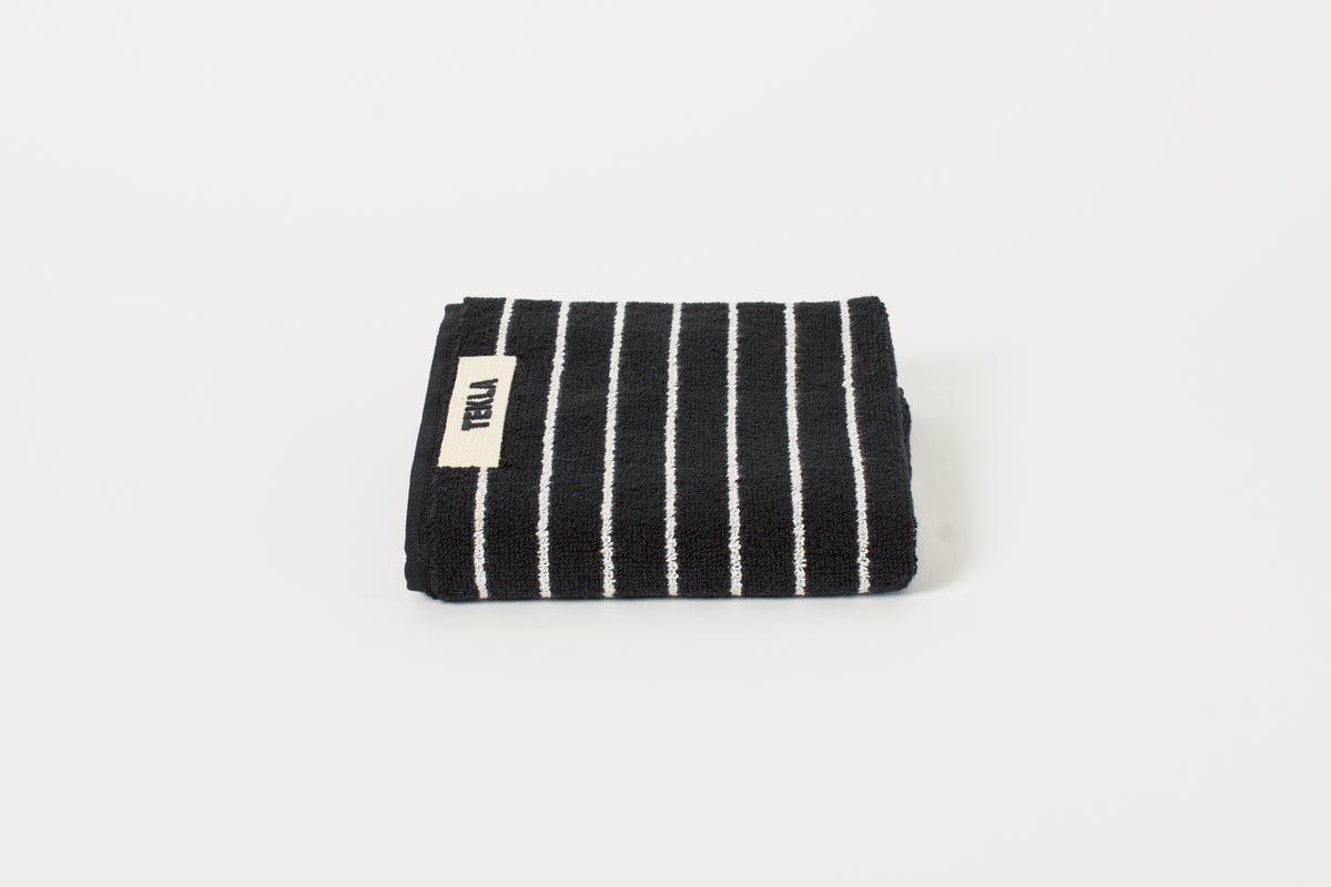 A folded black and white striped guest towel with the brand label 'Tekla' visible on one corner.