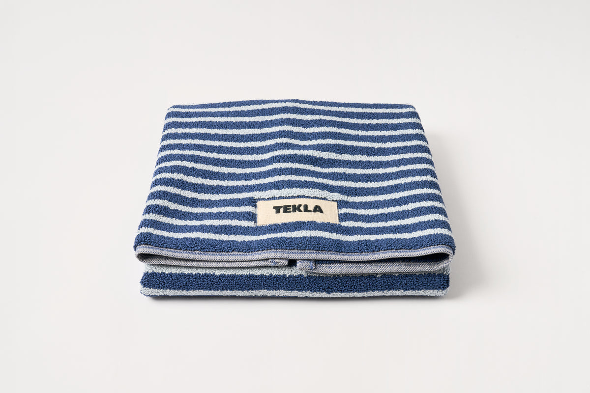 Folded blue and white striped towel with 'Tekla' label on a light gray background