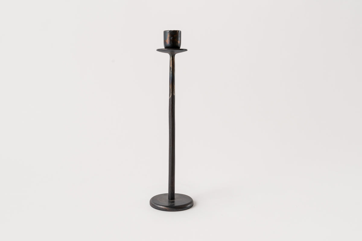 A black iron tapered candle holder with a flat base and a small holder at the top for a candle.