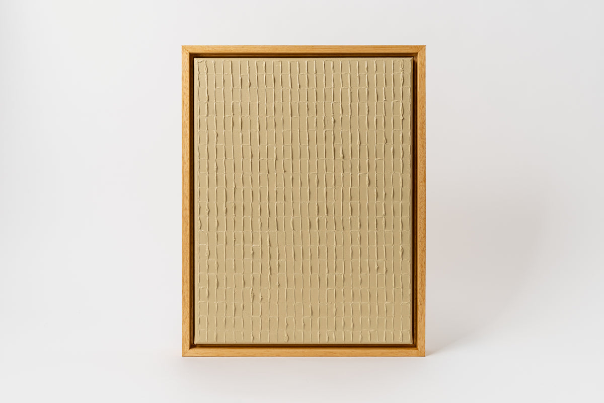 A framed artwork featuring a beige and brown textured canvas in a simple wooden frame, with the artist's signature in the lower right corner.