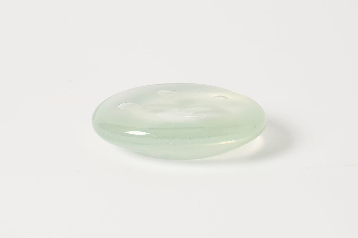 A smooth, oval-shaped translucent light green stone cabochon with a polished finish, resting on a plain white surface.