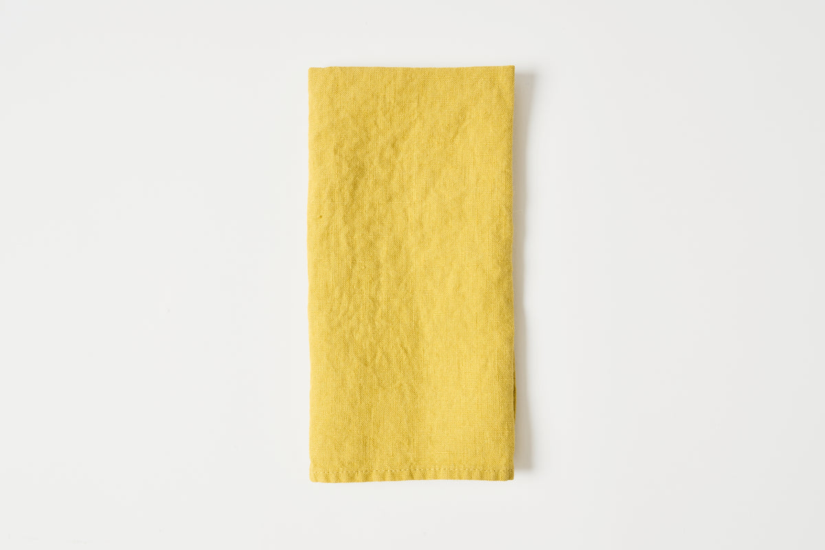 A folded yellow fabric napkin or tea towel with a textured, linen-like surface, centered on a clean white background.