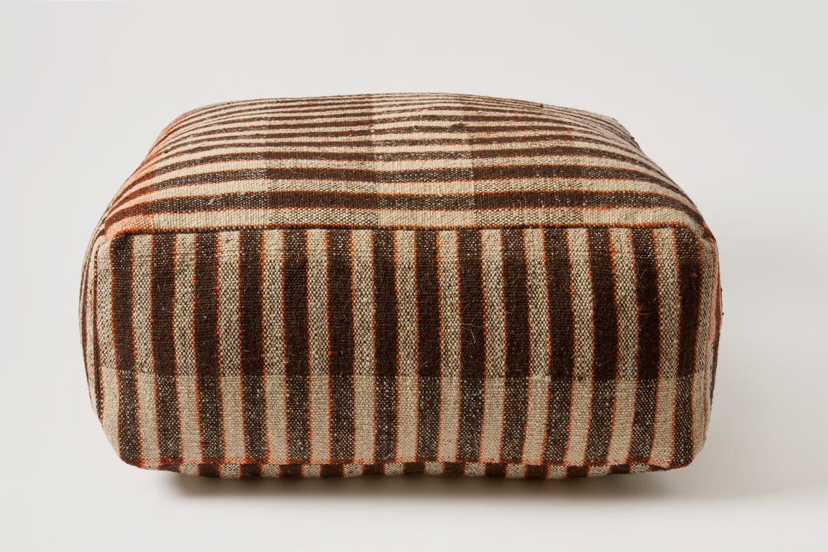 A square upholstered ottoman or pouf with a vertical striped pattern in dark brown, beige, and muted orange, shown against a plain light gray background.