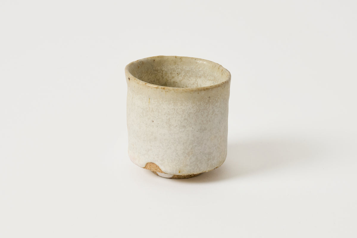 A small handmade ceramic cup with a textured, speckled off-white glaze and a slightly uneven rim, photographed on a clean white background.