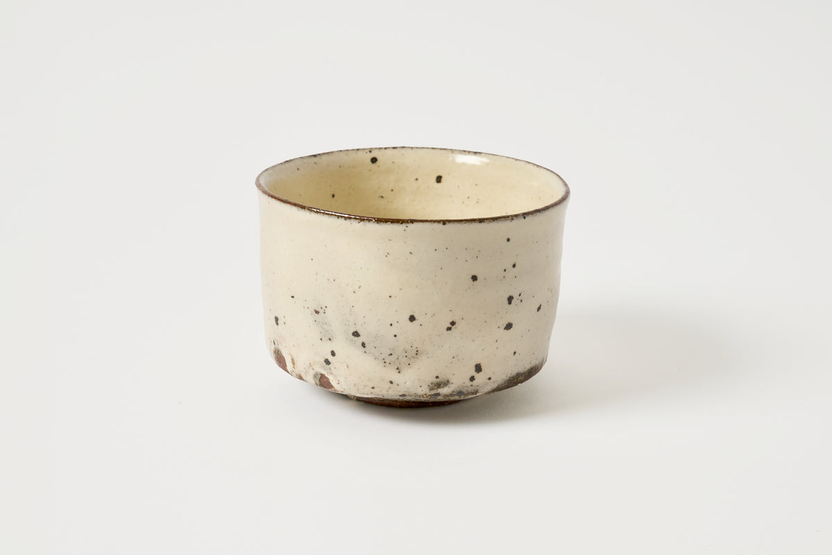 A handmade ceramic cup with a speckled cream and brown glaze, photographed on a clean white background.