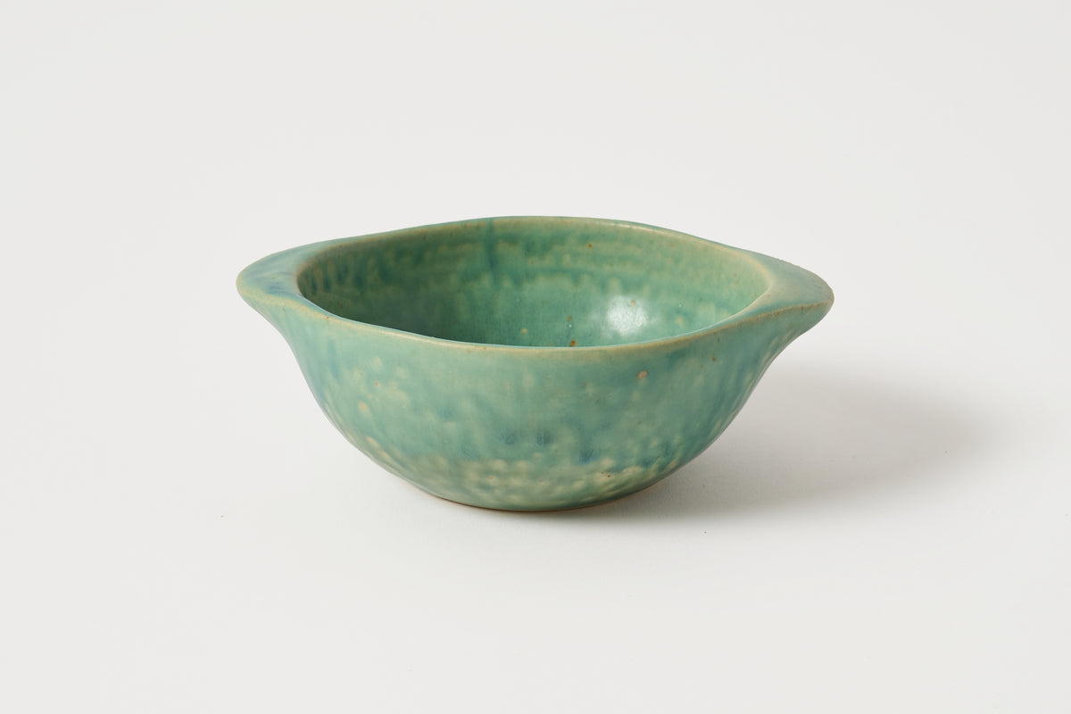 A small ceramic bowl with a textured, speckled green glaze and flared handles, photographed on a clean white background.