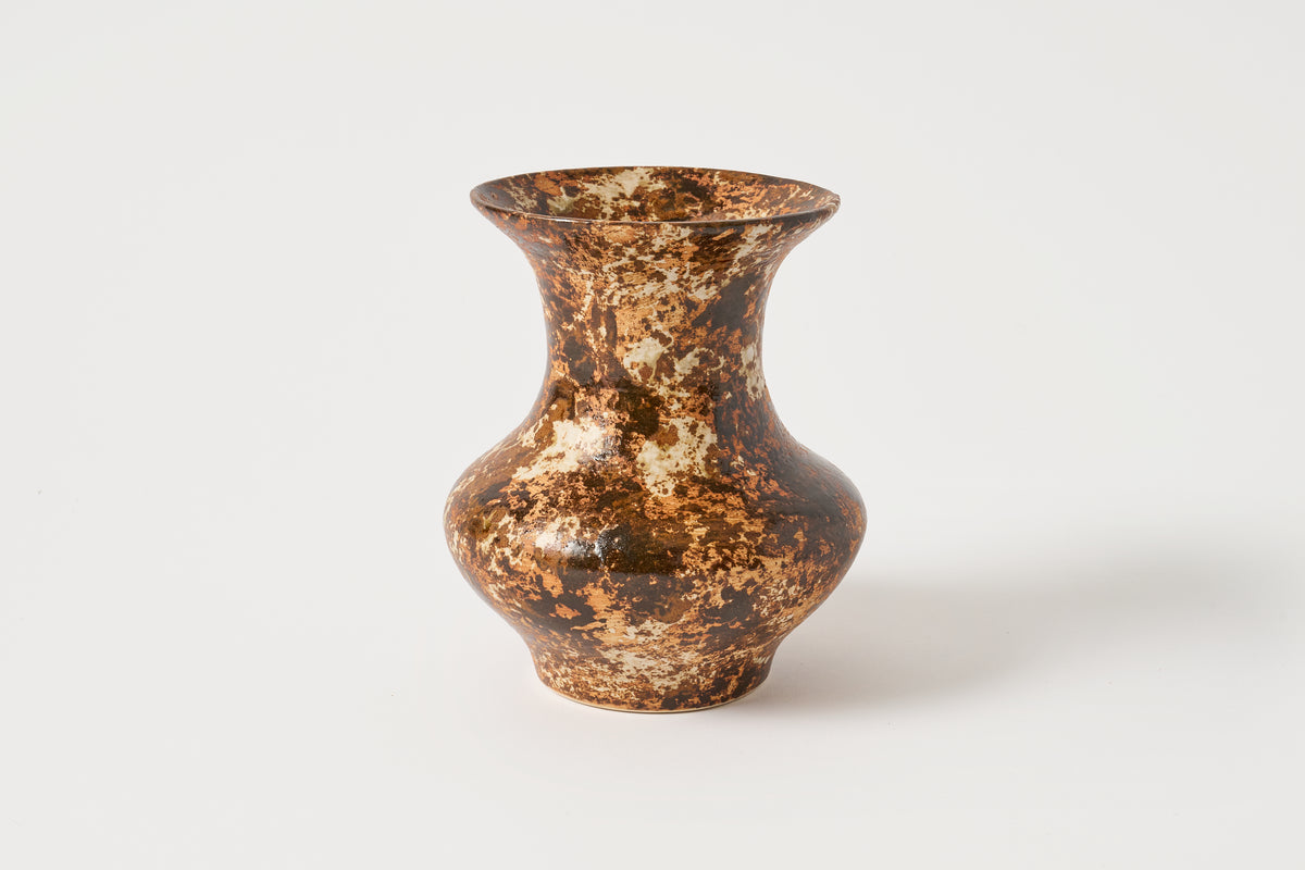 A small ceramic vase with a bulbous body and flared rim, featuring a mottled metallic gold and dark brown glaze, set against a plain light gray background.