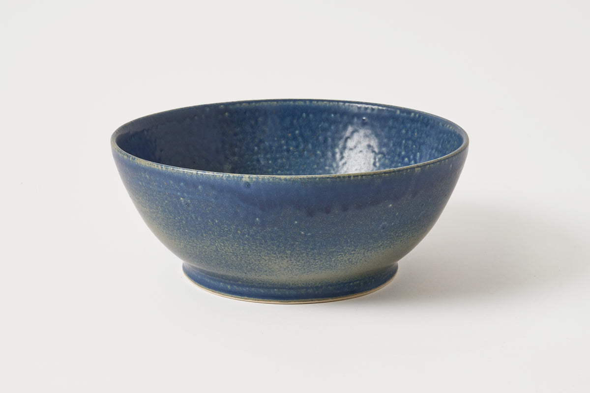 A handmade ceramic bowl with a textured, speckled blue glaze, photographed on a clean white background.
