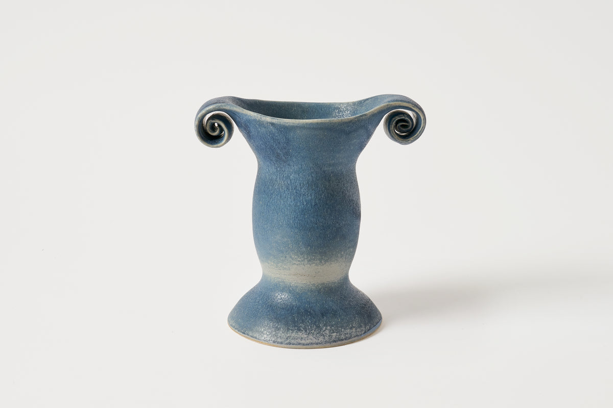 A small blue ceramic vase with a flared base and two curled handles, photographed on a clean white background.