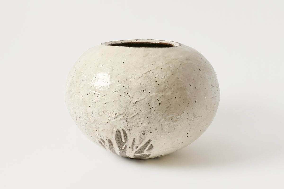 A small round ceramic vase with a textured, speckled off-white glaze and a small leaf motif near the base, photographed on a clean white background.