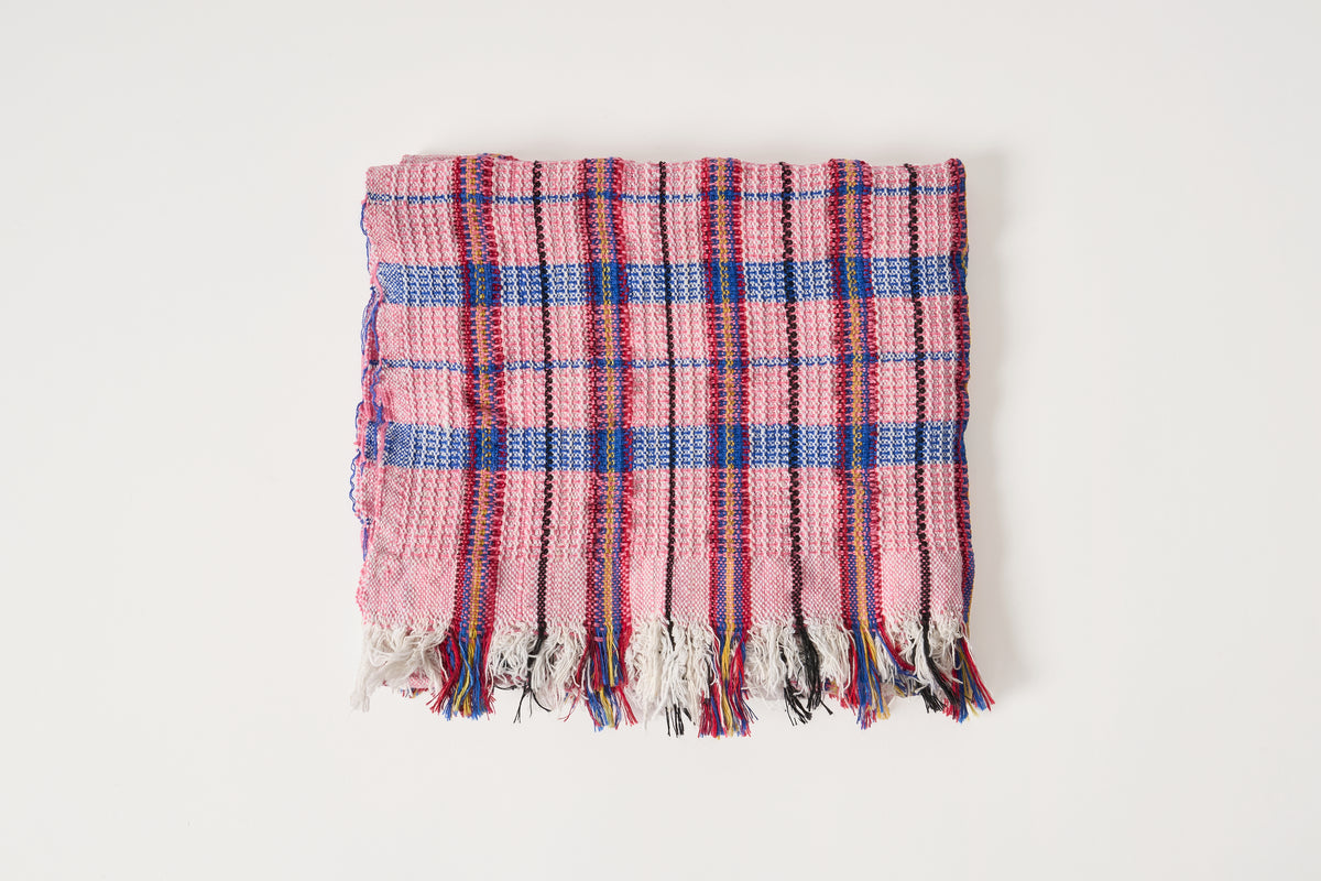 A folded woven throw blanket with a pink, blue, and red plaid pattern and fringed edges, displayed on a clean white background.