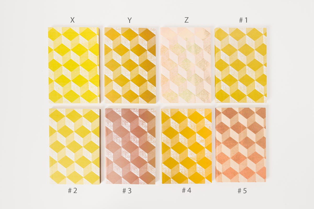 Stack of Astier de Villatte medium notebooks with geometric patterns in beige, yellow, and pink colors.