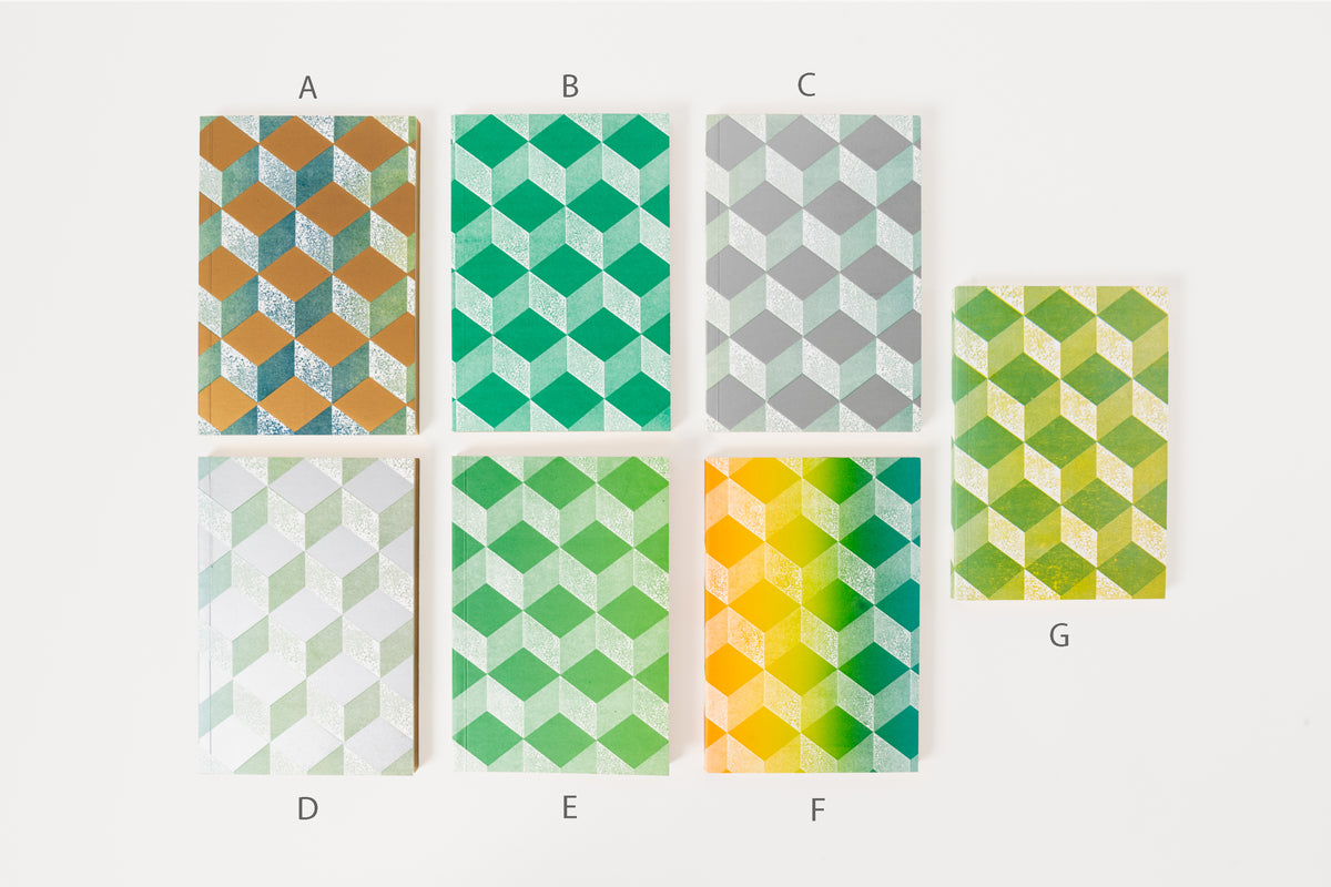 Stack of Astier de Villatte medium notebooks with geometric patterns in grey, green, and gold colors.