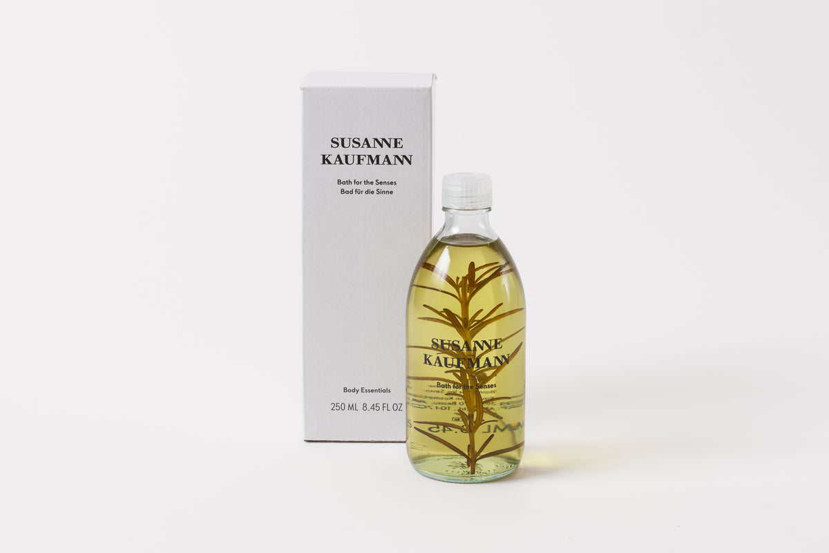 A clear bottle with a yellow liquid and a sprig of rosemary, next to its packaging box which reads 'Susanne Kaufmann'.