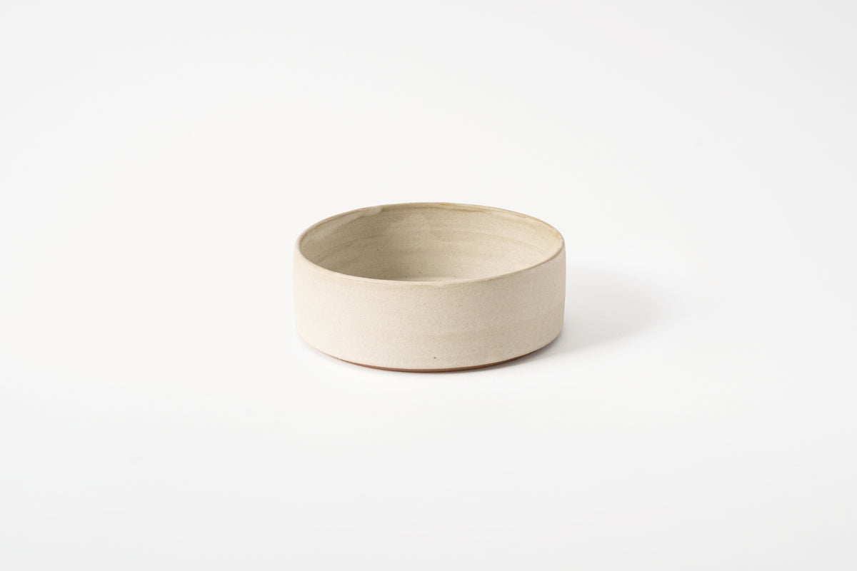 A matte white, wheelthrown ceramic bowl on a plain background.