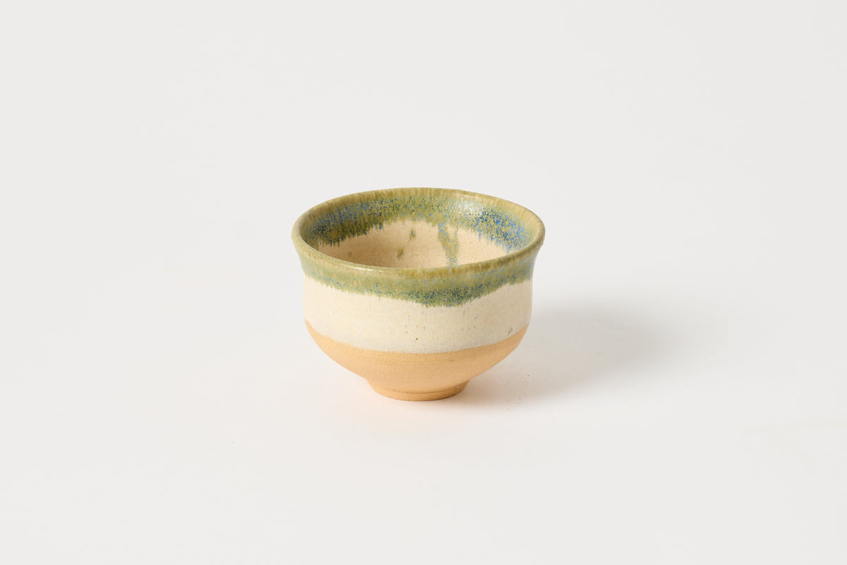 A small handmade ceramic tea bowl with a speckled green glazed rim and a natural beige clay base, photographed on a clean white background.