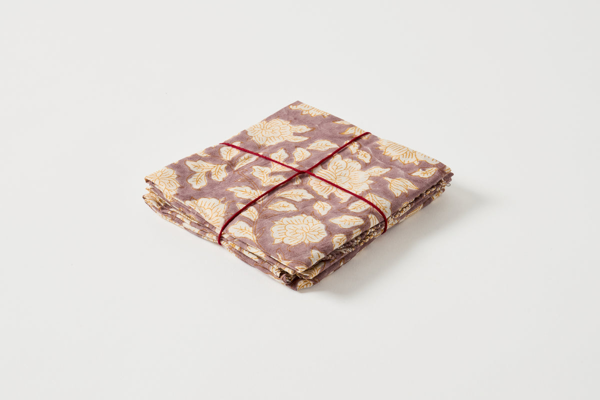 A folded fabric item, likely a napkin or small cloth square, featuring a muted mauve and beige floral pattern, tied with a thin red string on a clean white background.