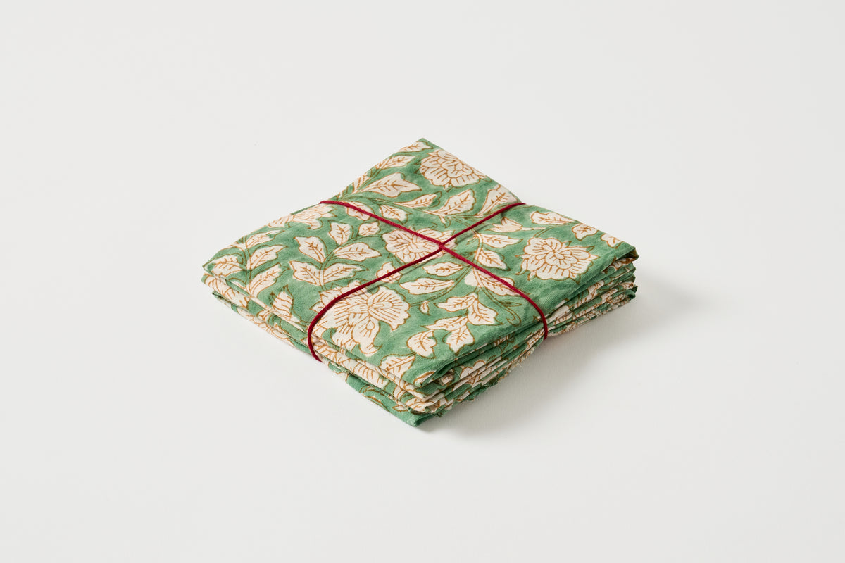 A folded green fabric item with a beige floral block print pattern, tied with a red string, on a light gray background.