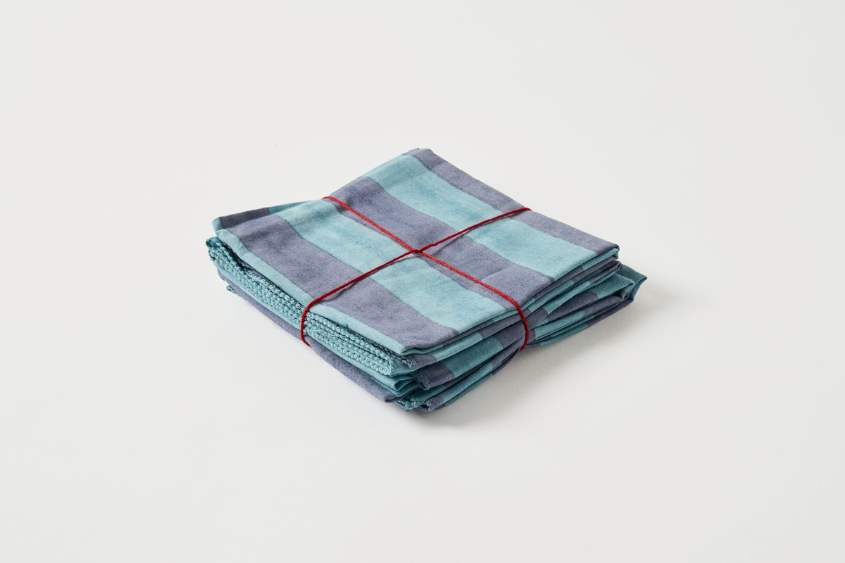 A stack of folded striped kitchen towels in shades of teal, blue, and purple, tied with a red string, on a light gray background.