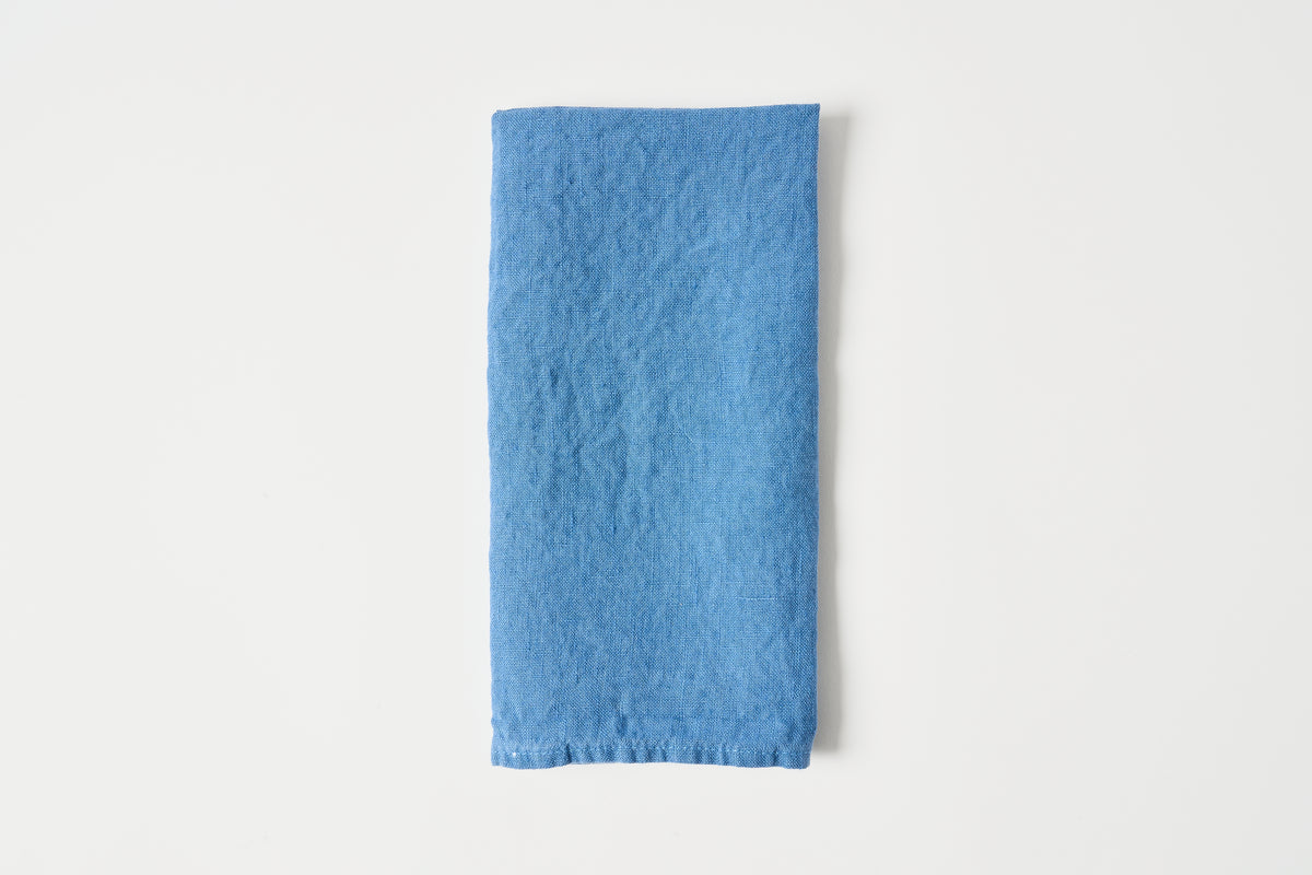 A folded blue fabric napkin or cloth with a textured linen-like surface, centered on a clean white background.