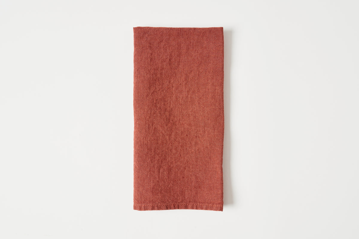 A folded terracotta-colored linen napkin with a visible woven texture, centered on a clean white background.