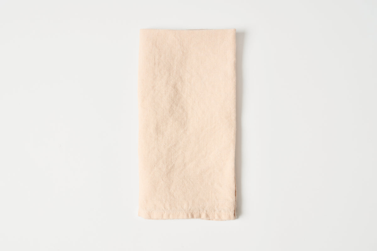A folded, light peach-colored linen napkin with a natural, slightly textured surface, centered on a clean white background.