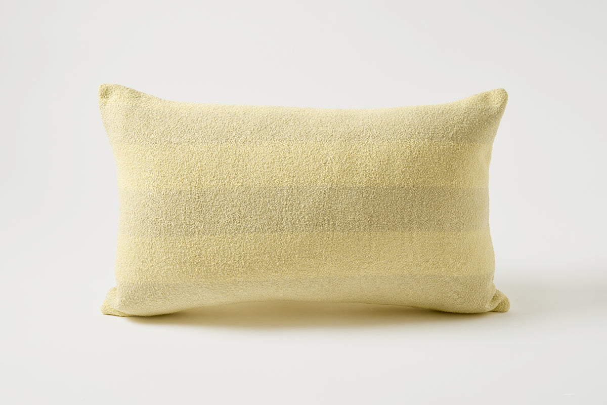 A pale yellow textured lumbar pillow with subtle horizontal stripes, photographed on a clean white studio background.