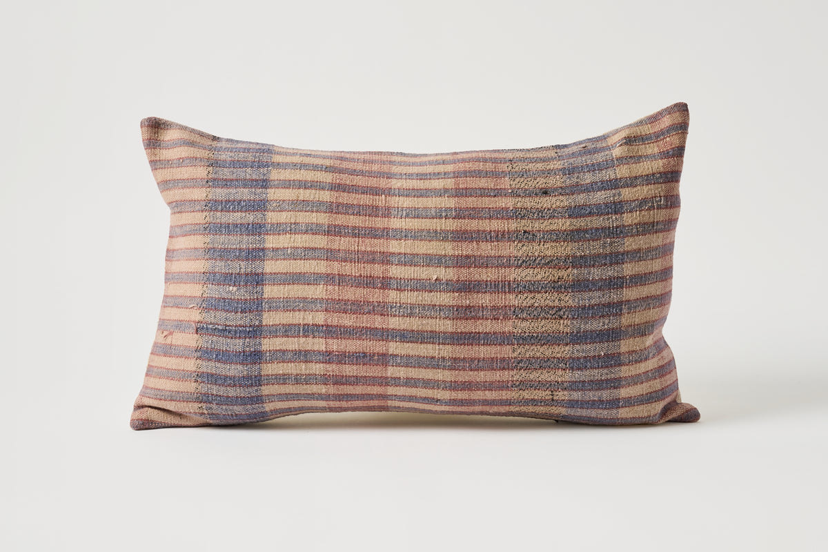 A rectangular lumbar throw pillow with a rustic striped pattern in muted shades of blue, brown, and beige, set against a plain light gray background.
