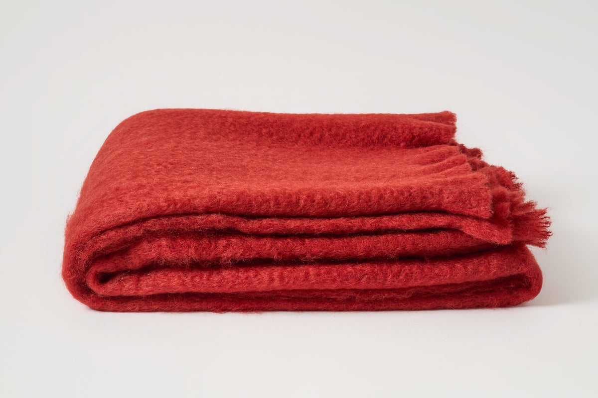 A folded red knit throw blanket with fringed edges, displayed on a clean white background.