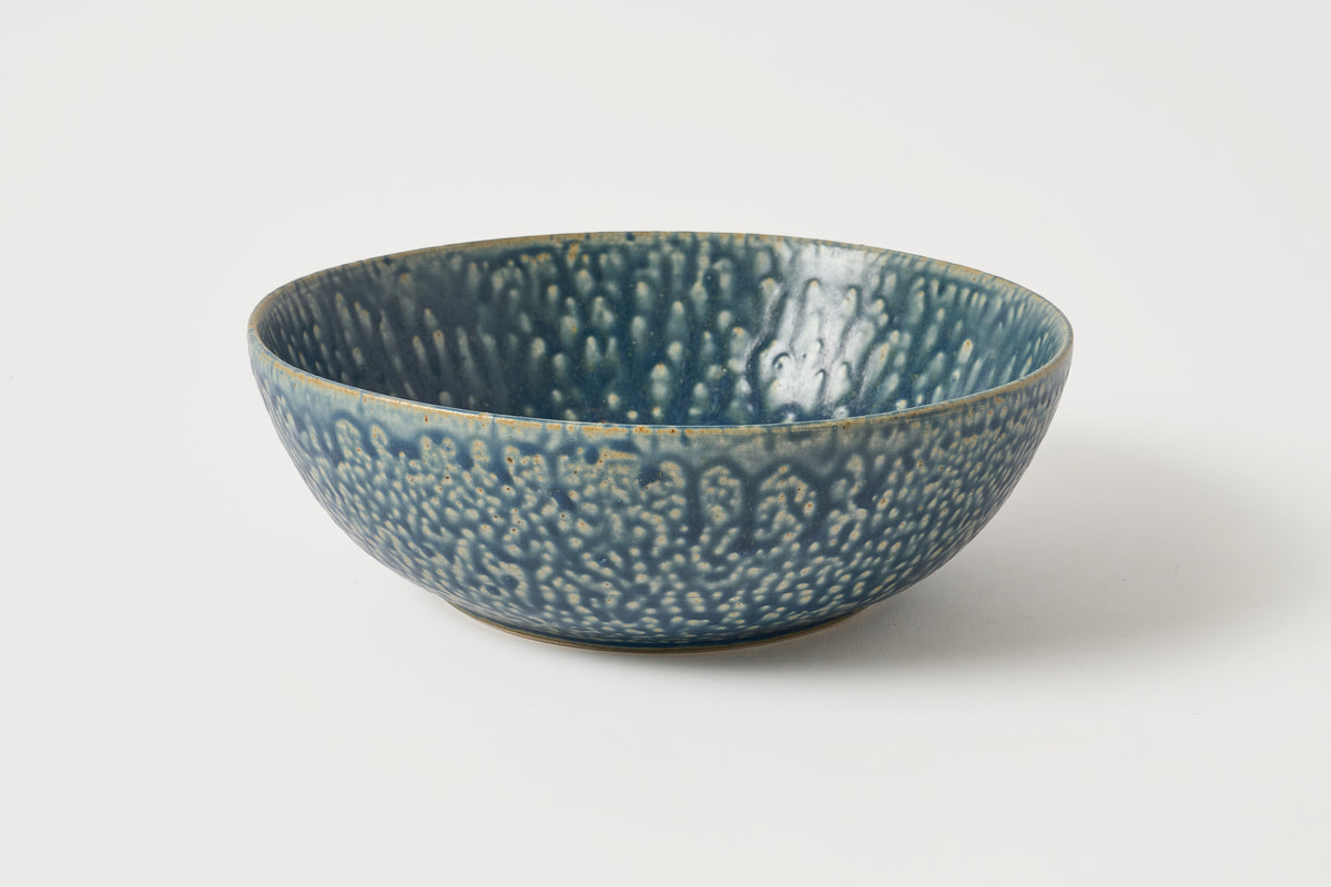 A handmade ceramic bowl with a textured, hammered glaze in a deep teal blue color, shown on a clean white background.