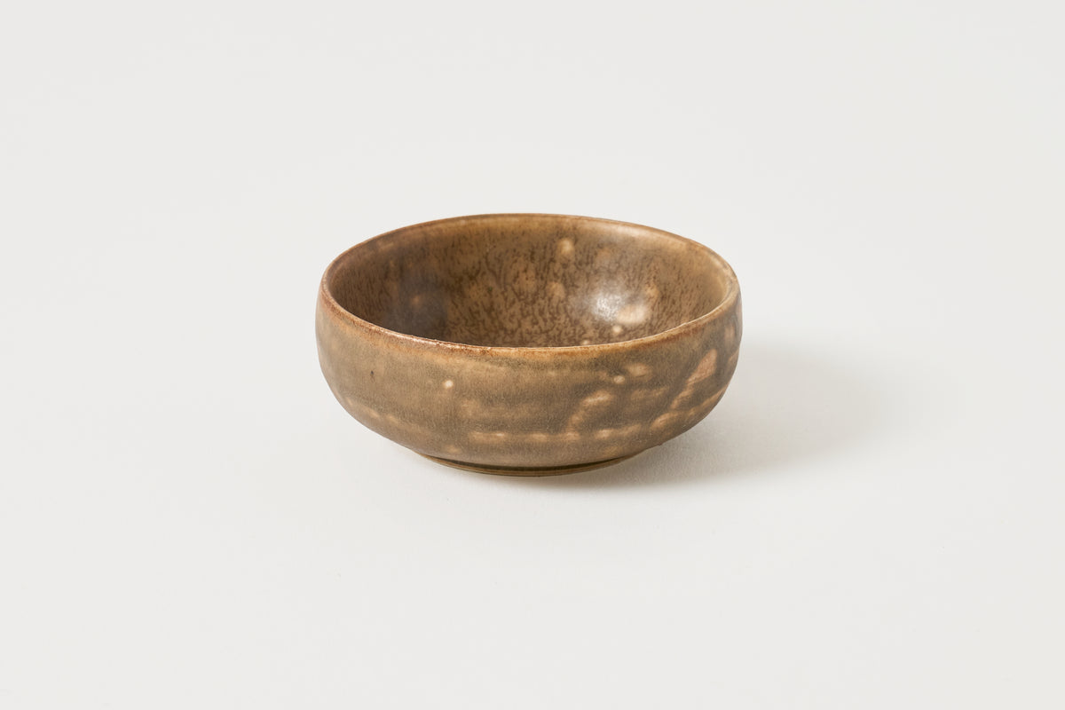 A small handmade ceramic bowl with a textured, speckled brown and beige glaze, photographed on a clean white background.
