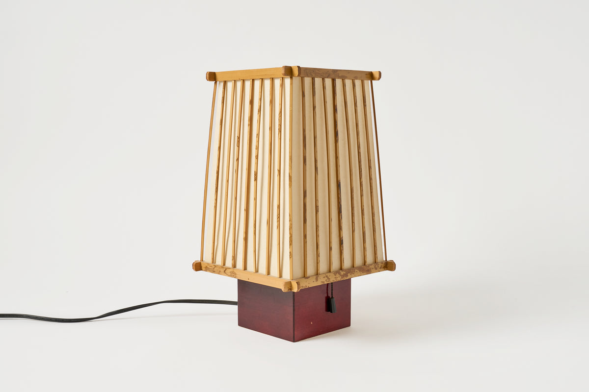A mid-century modern table lamp featuring a slatted bamboo shade, a dark reddish-brown wooden base, and a black power cord, shown against a plain white background.