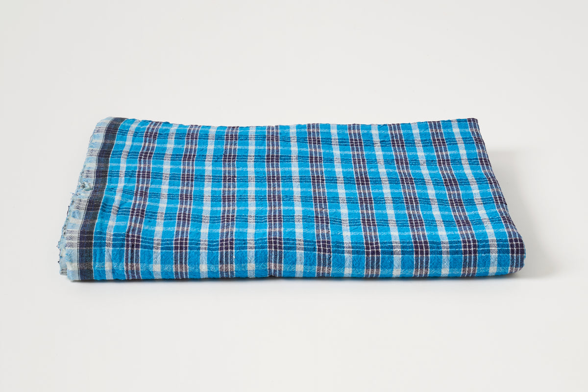 A folded plaid fabric item, likely a scarf or bandana, featuring a bright blue, white, and dark navy checkered pattern on a clean white background.