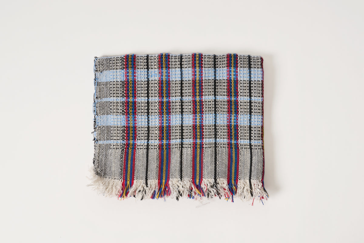 A square woven towel with a gray and white plaid pattern and multicolored striped fringe, displayed flat against a plain off-white background.