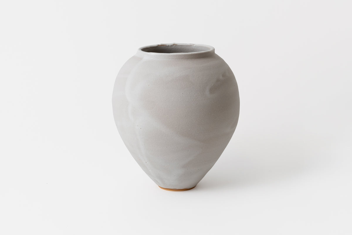 A hand thrown ceramic vase with a frosted lilac finish and a wooden base.