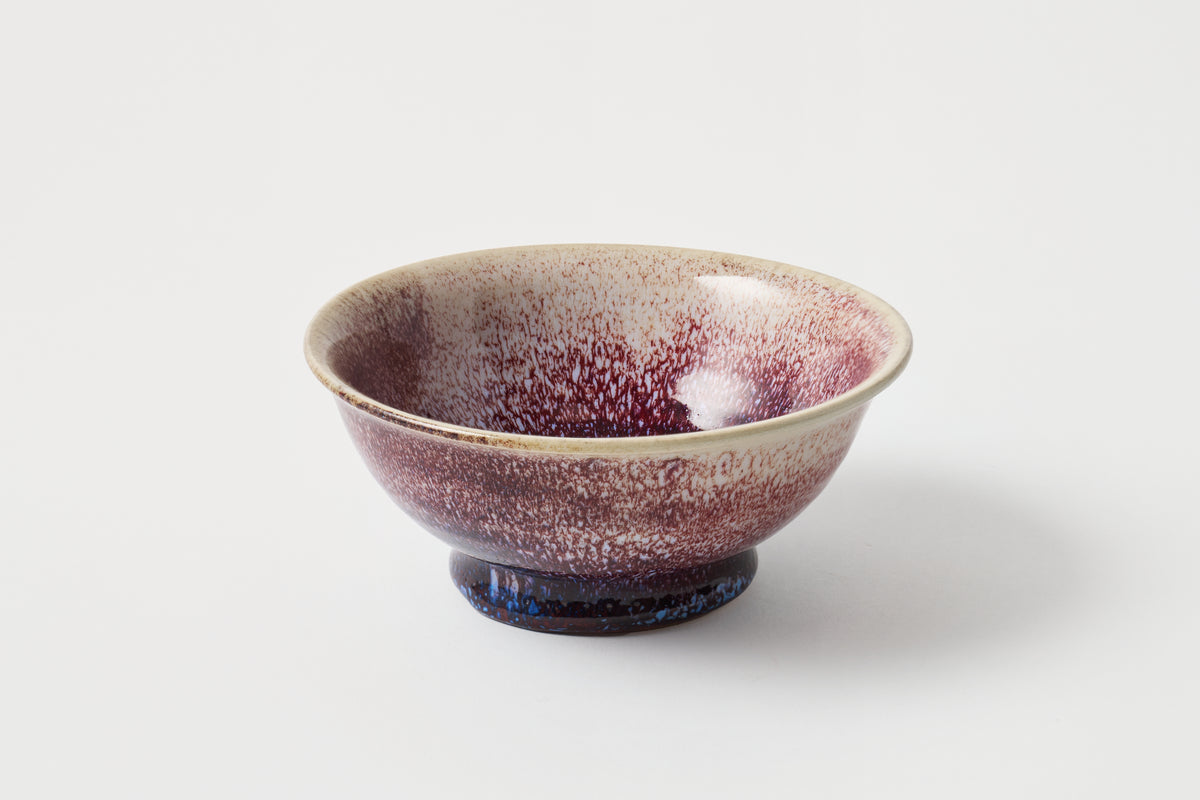 Ceramic bowl with purple speckled glaze on a white background