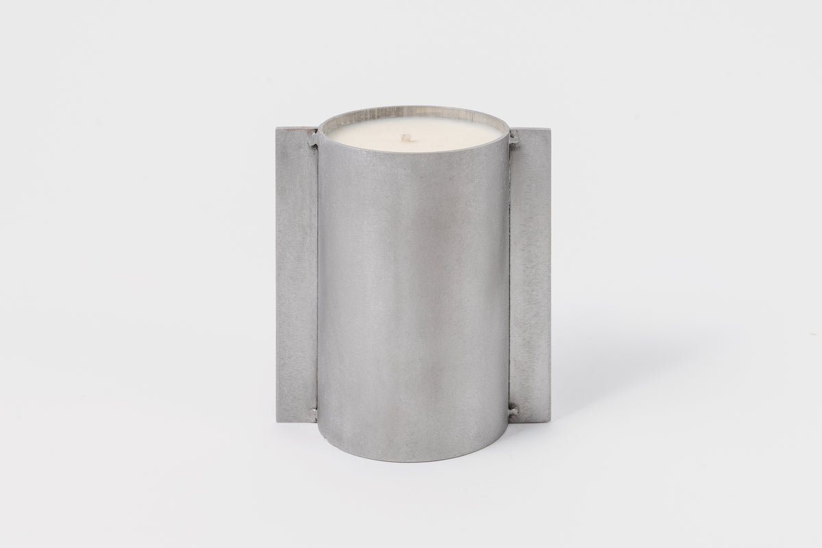 A cylindrical soy wax candle with a metallic silver finish and an organic cotton wick, designed by FDK Floral in collaboration with John Wells.
